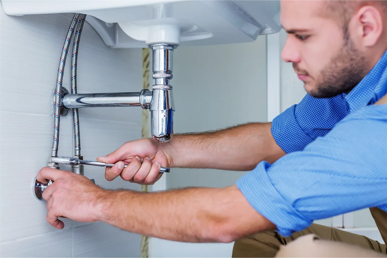 Professional plumber repairing under-sink plumbing connections with a wrench in New York