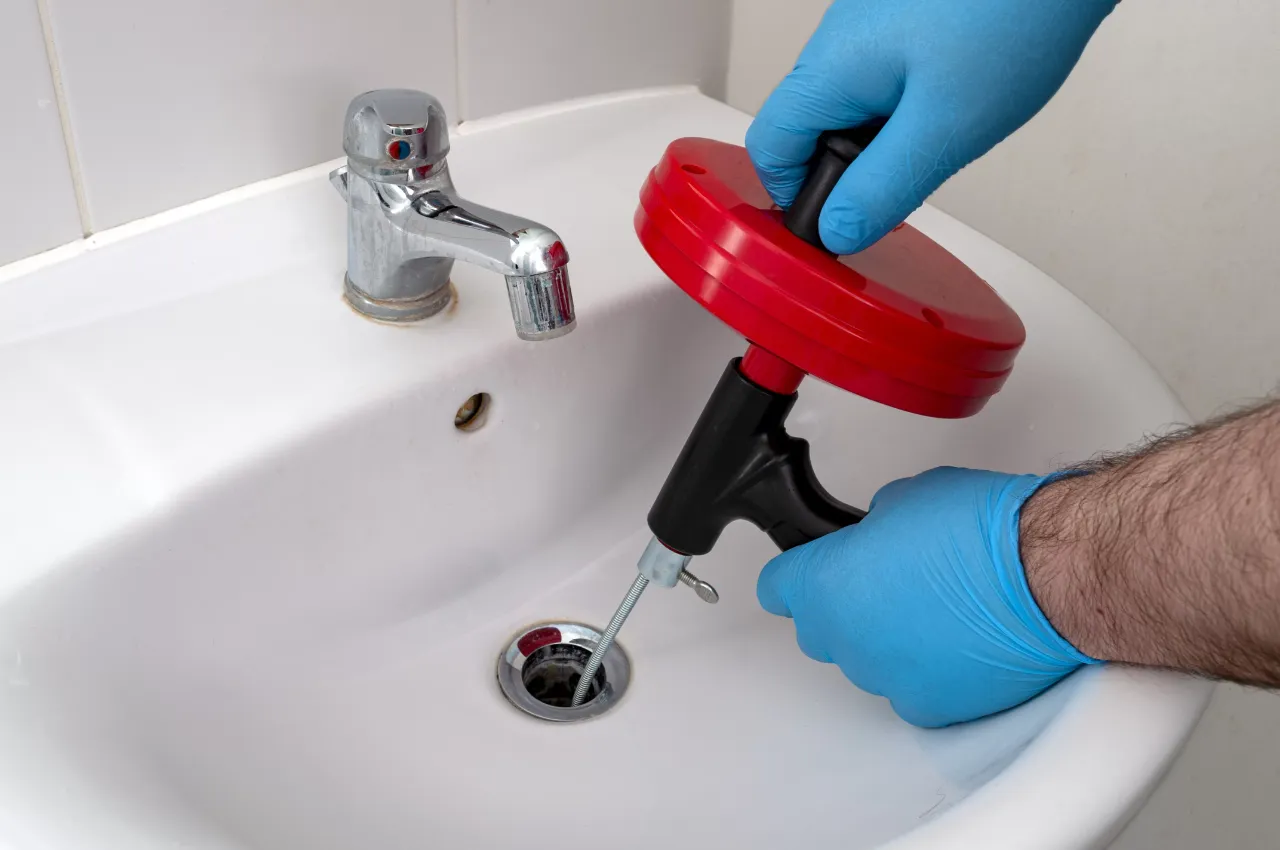 Professional plumber clearing a clogged bathroom sink drain with a drain snake in New York