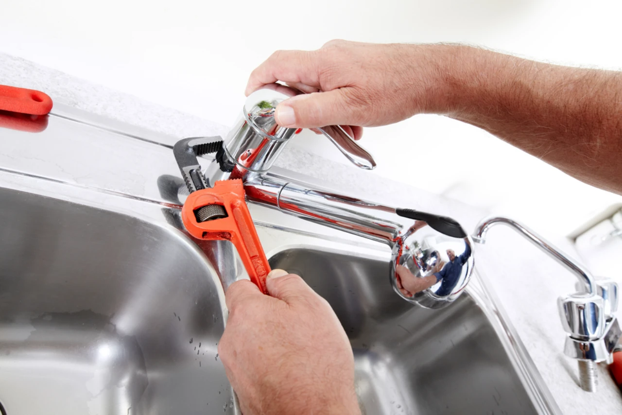Professional plumber replacing a kitchen faucet using adjustable wrenches over a sink in New York