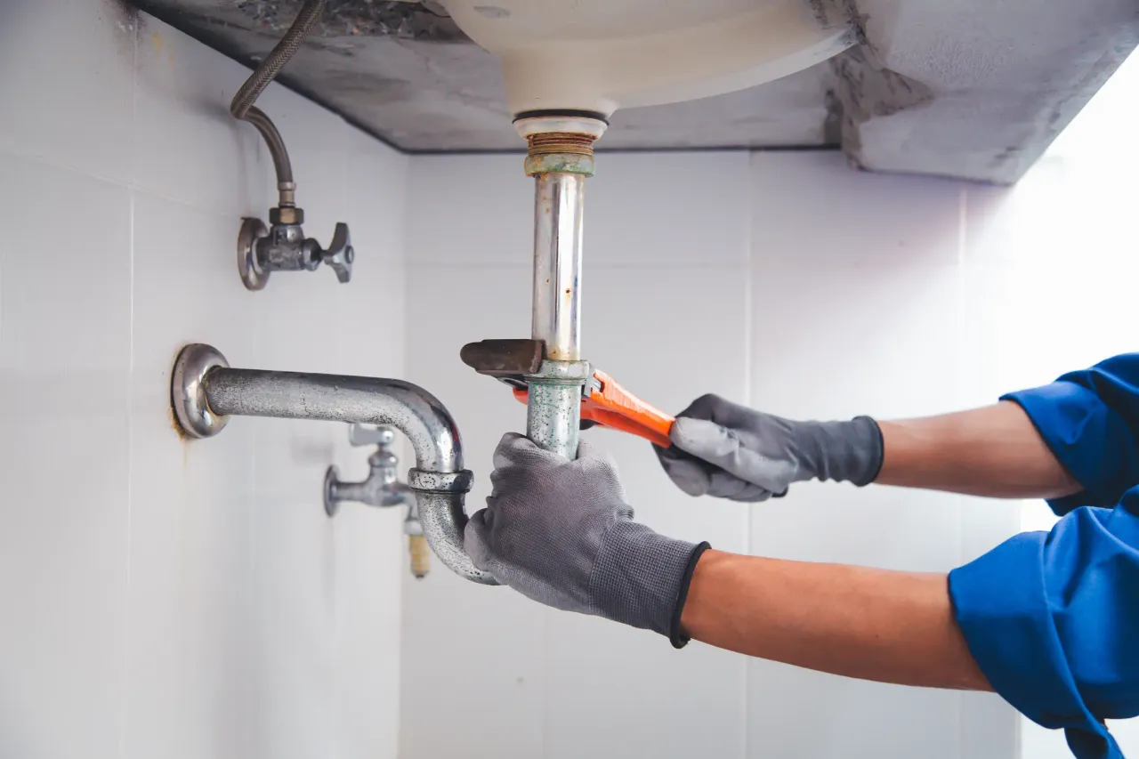 Professional plumber repairing a leaking sink drain pipe for water leak repair in New York