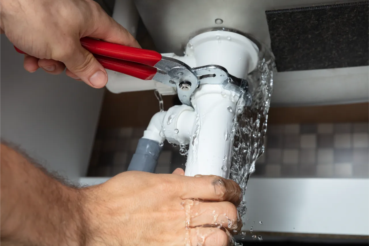 Professional plumber repairing a leaking pipe under a sink for water leak repair in New York