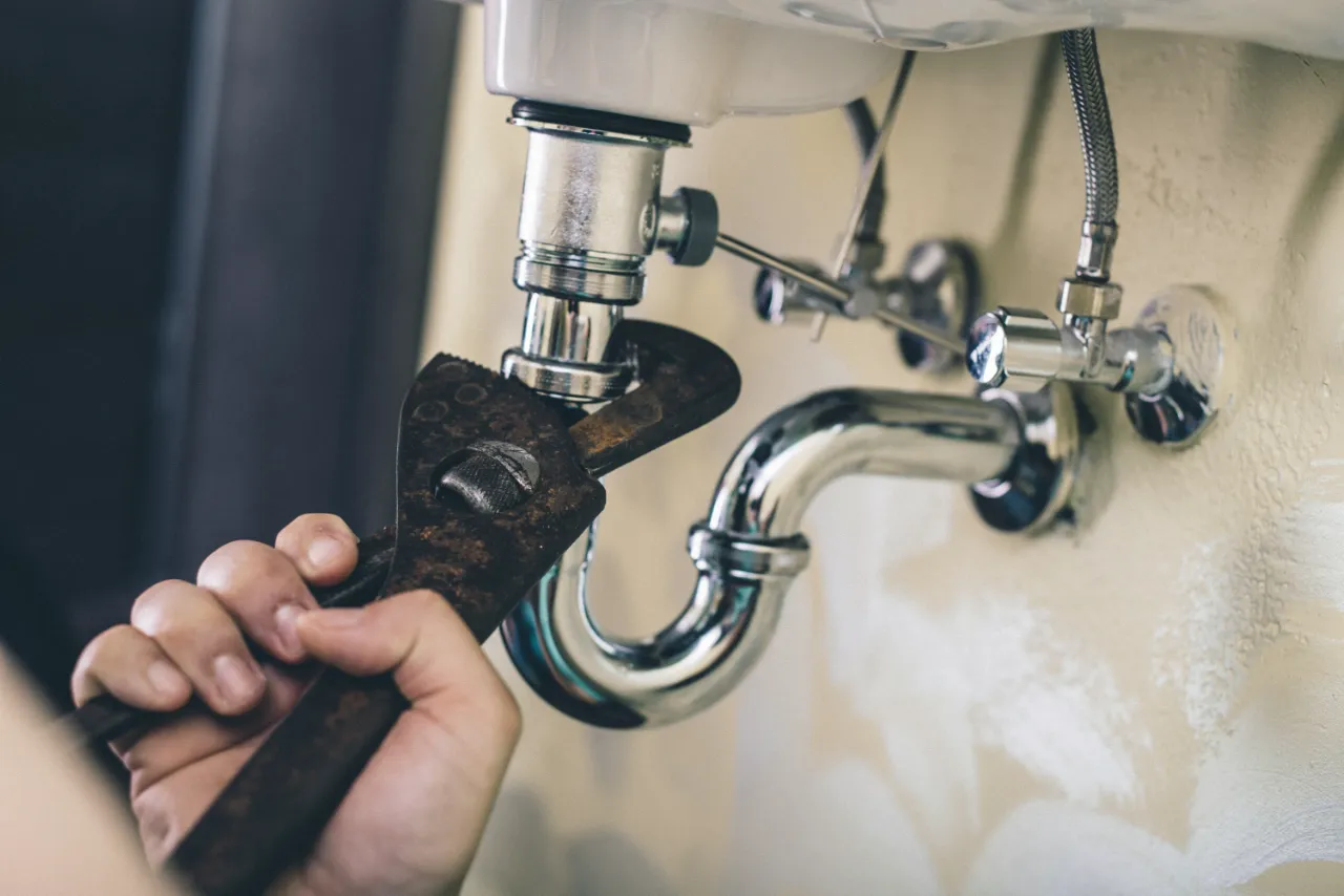 Professional plumber repairing under-sink plumbing with a wrench in New York